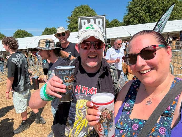 Steph and her friend Pete smiling and holding drinks in front of the bar tent earlier in the afternoon, before the crowd problems began.