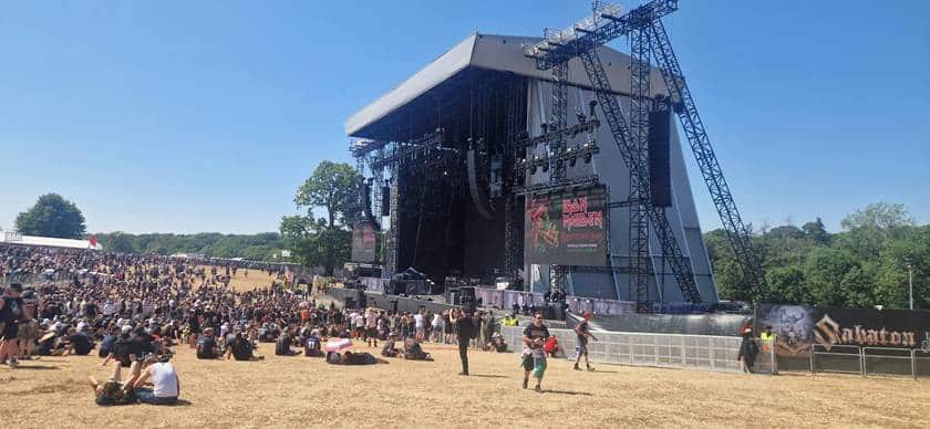 Wide shot of the main stage at EddFest in bright afternoon sunshine, with thousands of attendees gathered on the field.