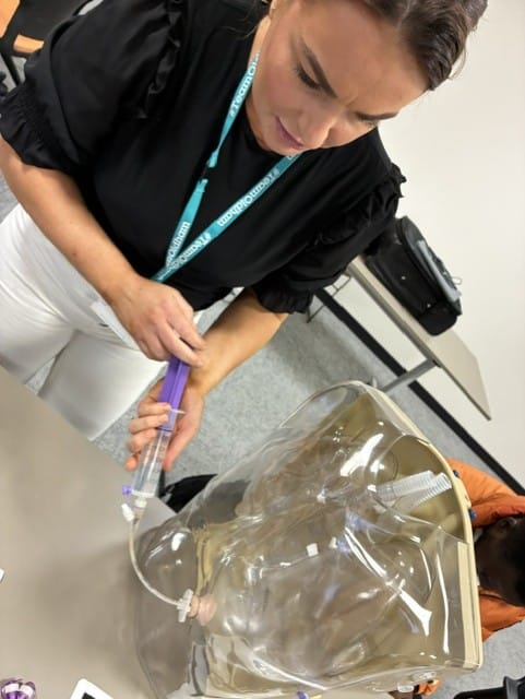 Care worker practising PEG feeding site care on a training model during a delegated healthcare activities course delivered in a care home by Prima Cura Training