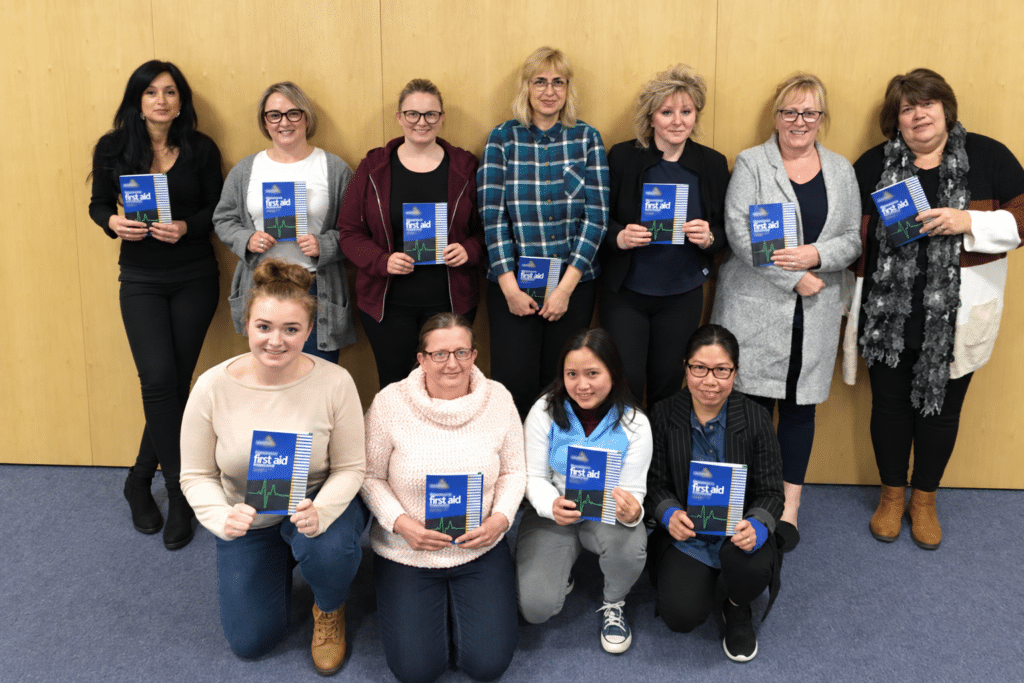 Staff from a Greater Manchester organisation holding their workbooks after completing Emergency First Aid at Work with Prima Cura Training