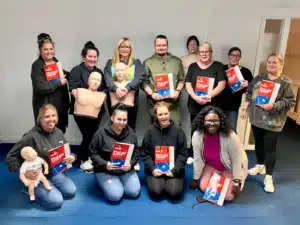 School staff practising paediatric first aid on a child manikin during on-site training delivered by Prima Cura Training in Bury, Greater Manchester