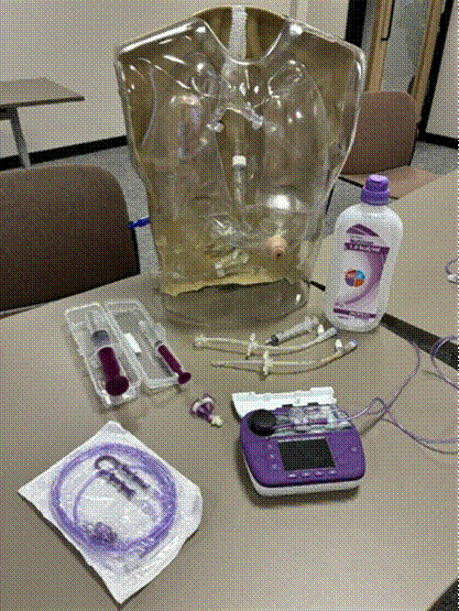 PEG training equipment laid out at a Prima Cura Training course: a clear training torso with a gastrostomy site, enteral syringes, a giving set, a bottle of Nutrison feed and an enteral feeding pump.